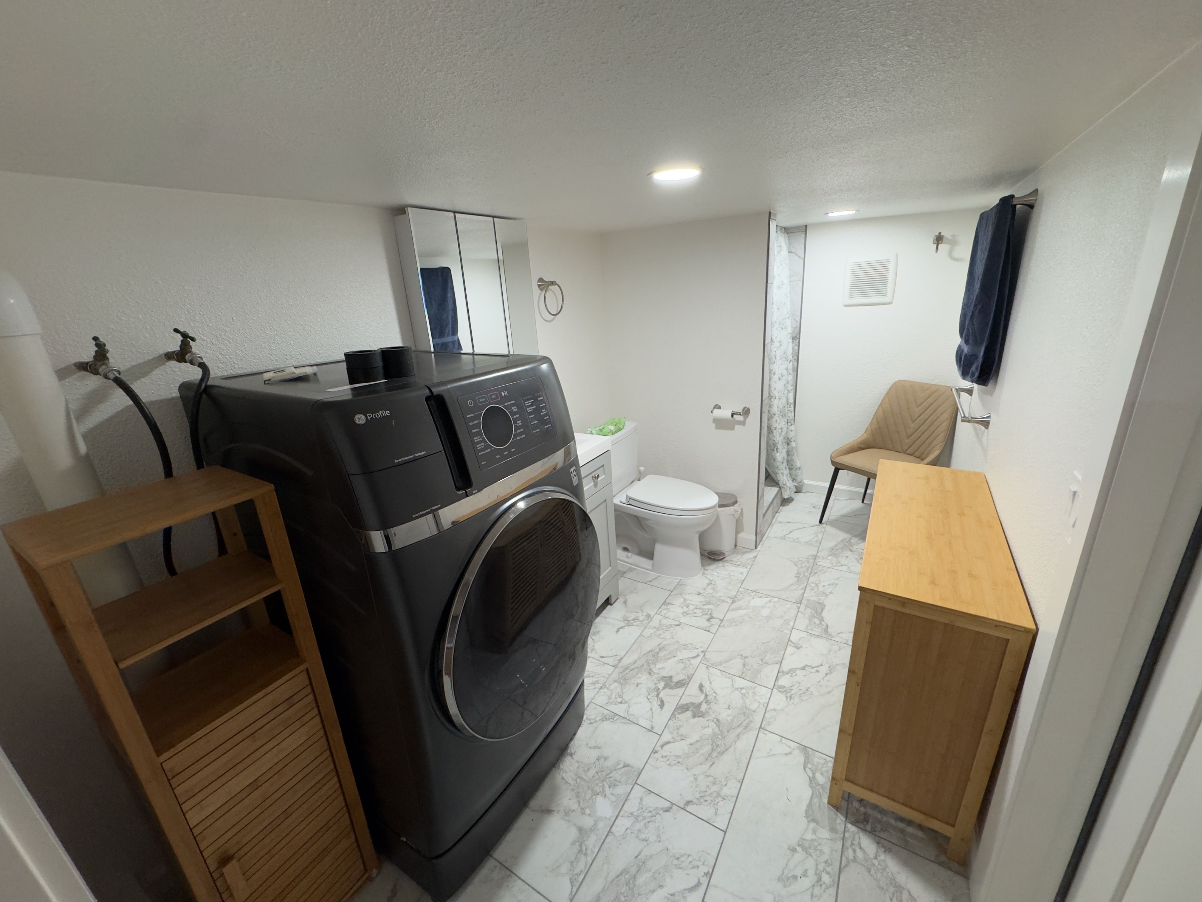 The ground-floor bathroom: antimicrobial tile floor, a full-size washer+dryer (2.5 hours wash+dry combined), toilet, and a tiled walk-in shower.